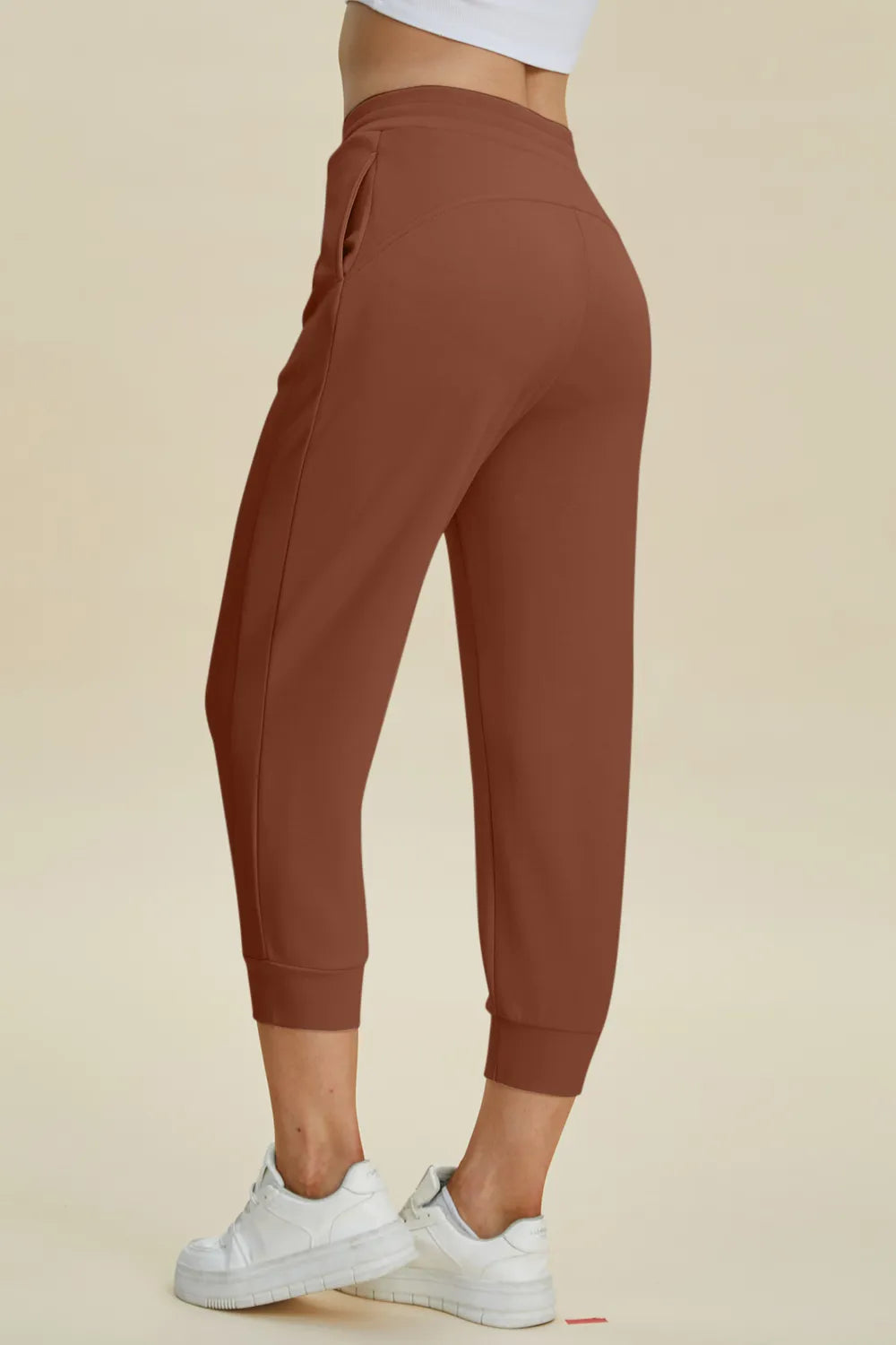 Brown jogger pants worn by a person on a beige background