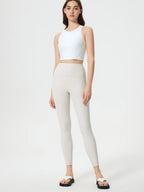 Woman wearing a white crop top and beige leggings on a white background
