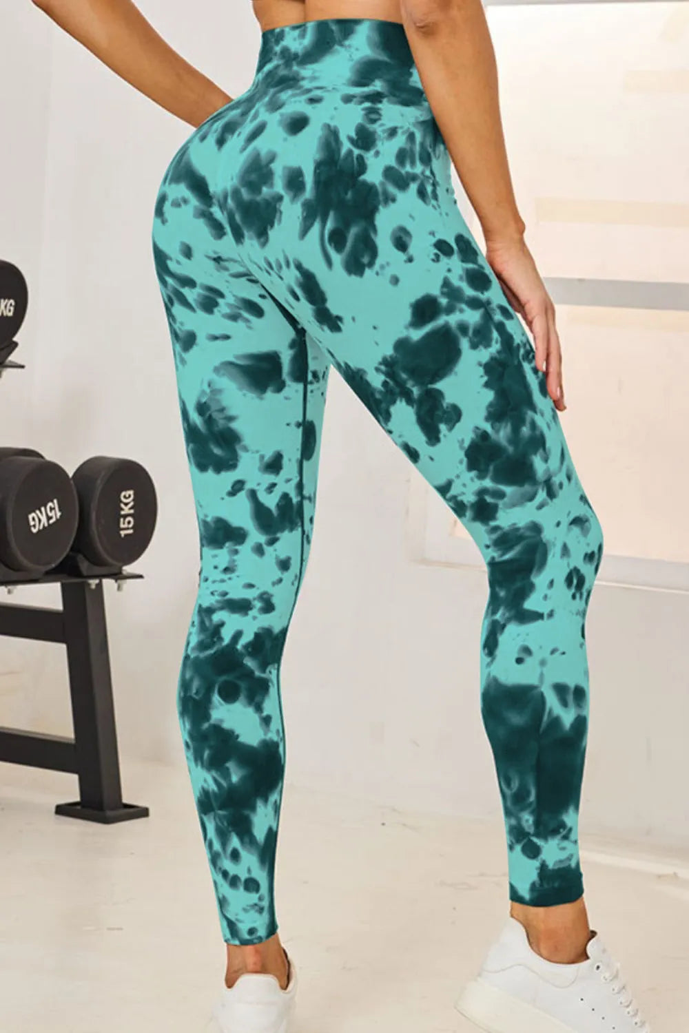 Person wearing teal tie-dye leggings in a gym setting with weights in the background.