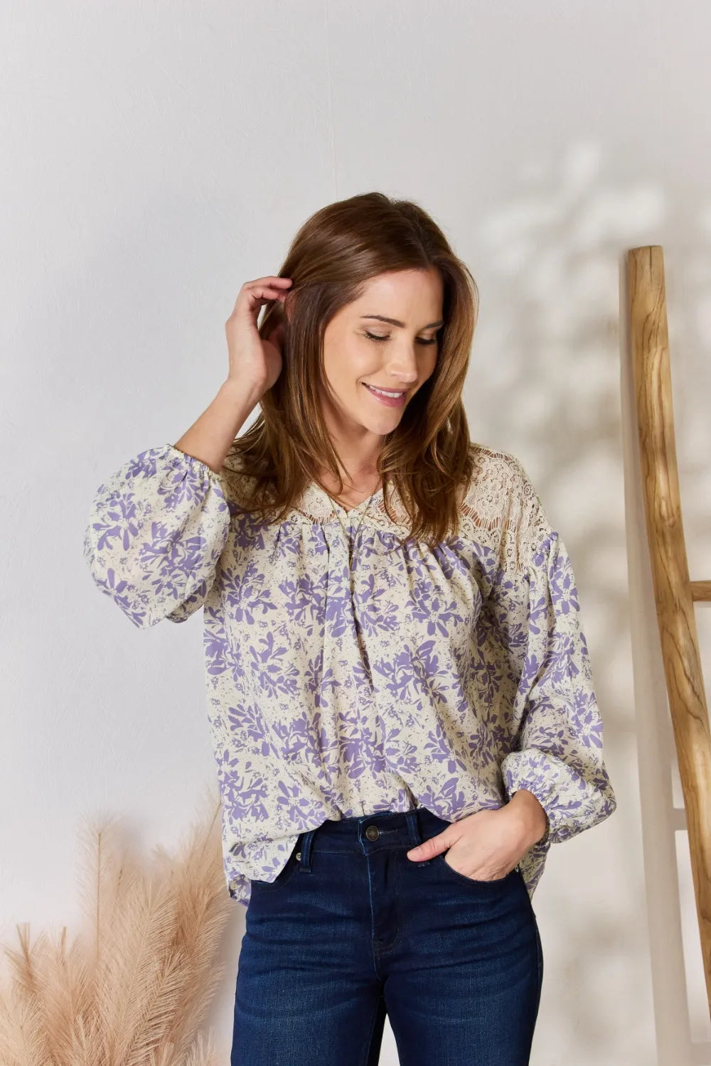 Woman wearing a floral blouse and blue jeans against a white wall.
