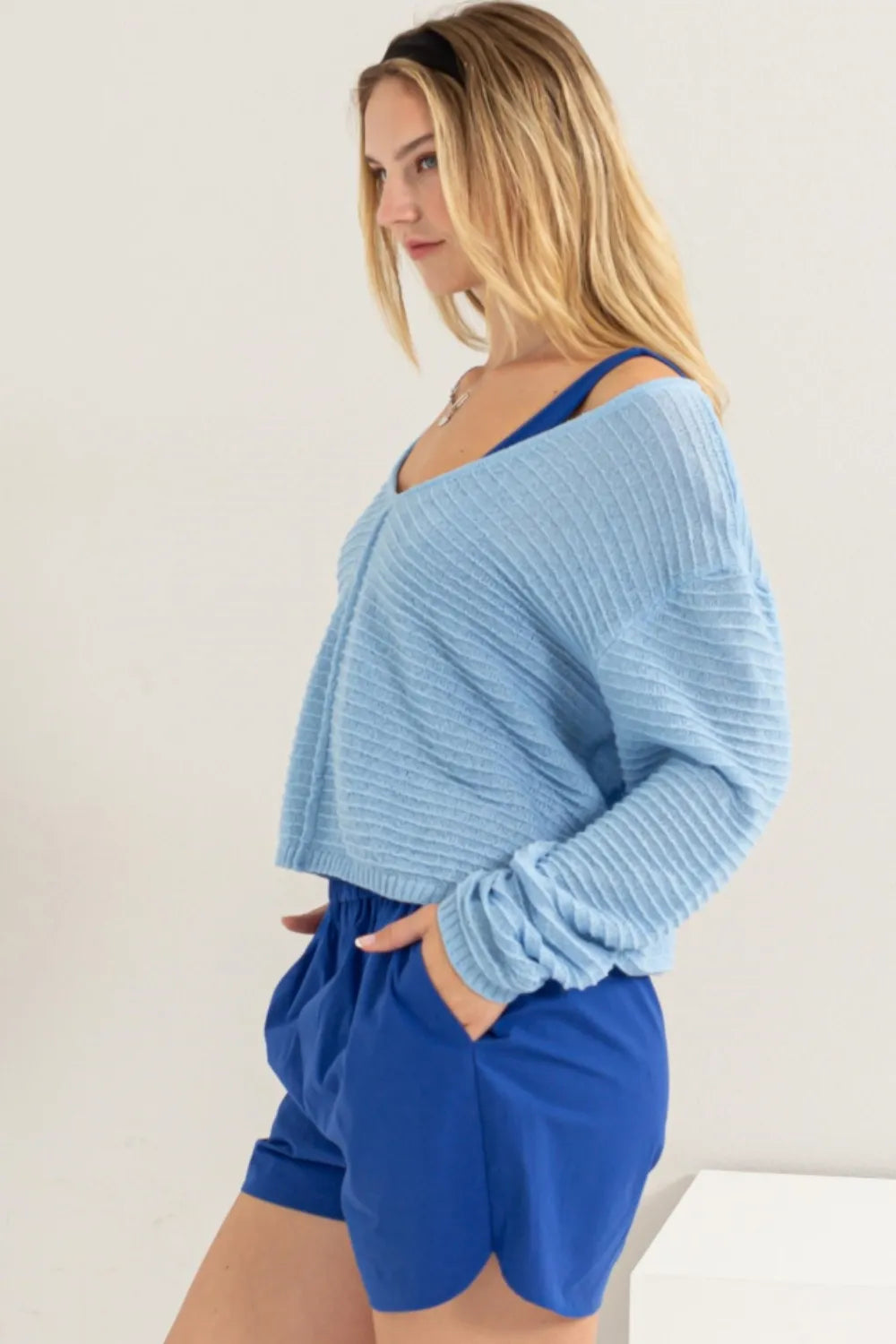 Woman wearing a light blue sweater and blue shorts against a plain background