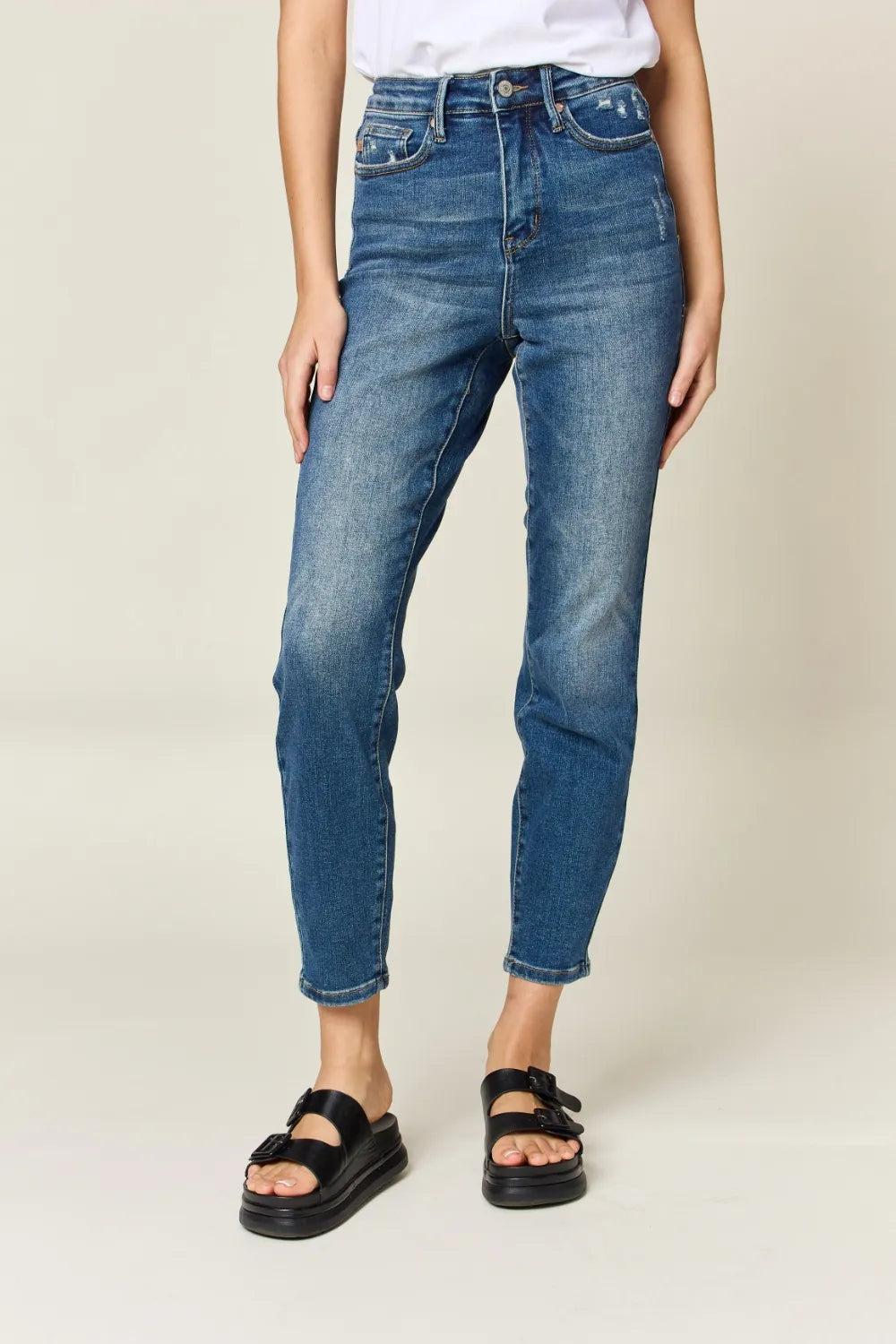 Person wearing blue jeans and black sandals on a plain background