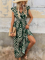 Woman wearing a green and white patterned dress with a straw hat and clutch.