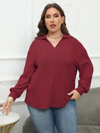 Woman wearing a burgundy ribbed sweater and blue jeans indoors.