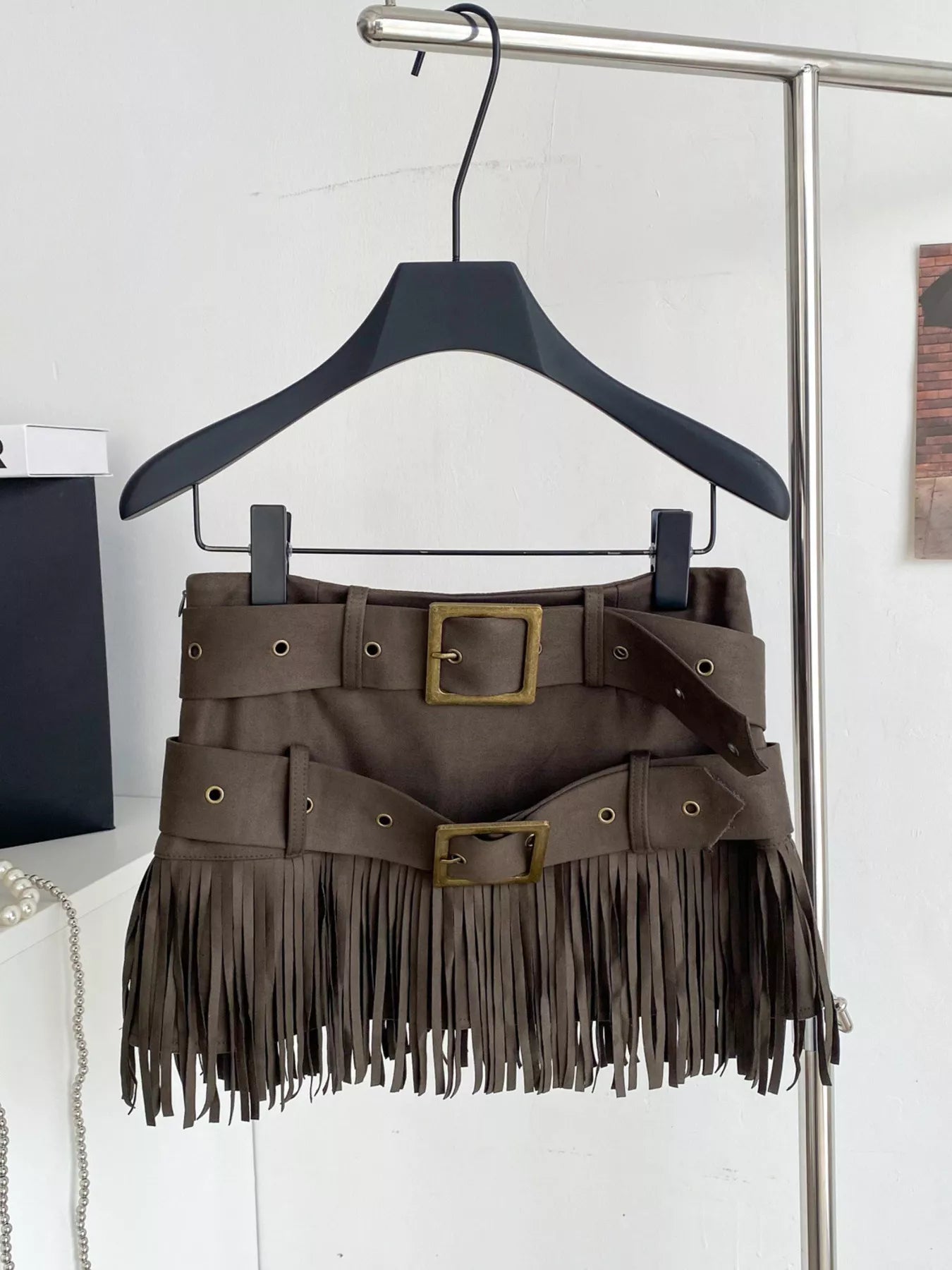 Brown fringe skirt with belt on a hanger against a white wall