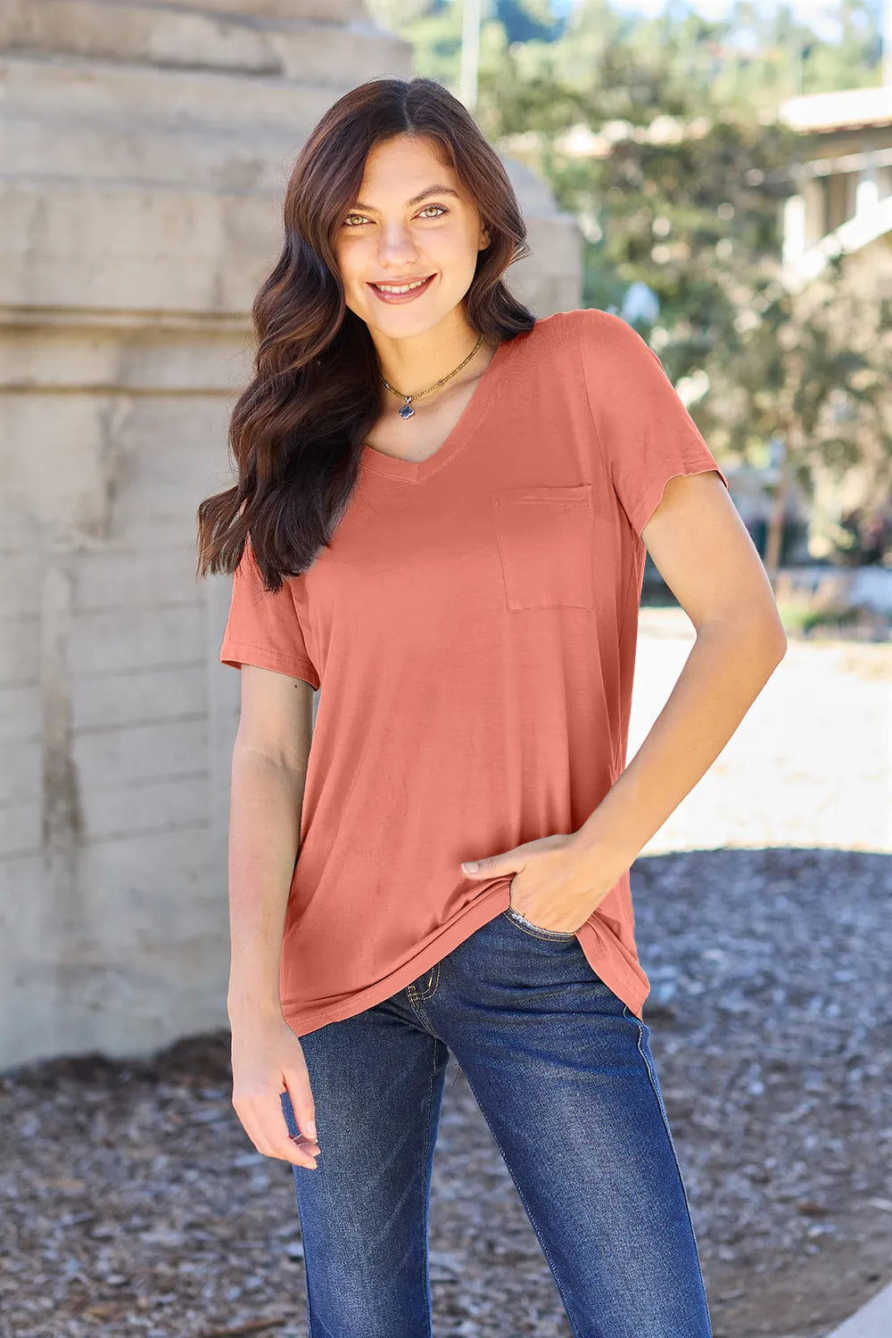 Woman wearing a terracotta-colored t-shirt with a pocket, standing outdoors.
