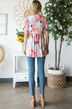 Person wearing a floral blouse and blue jeans standing in a room with a plant and table.