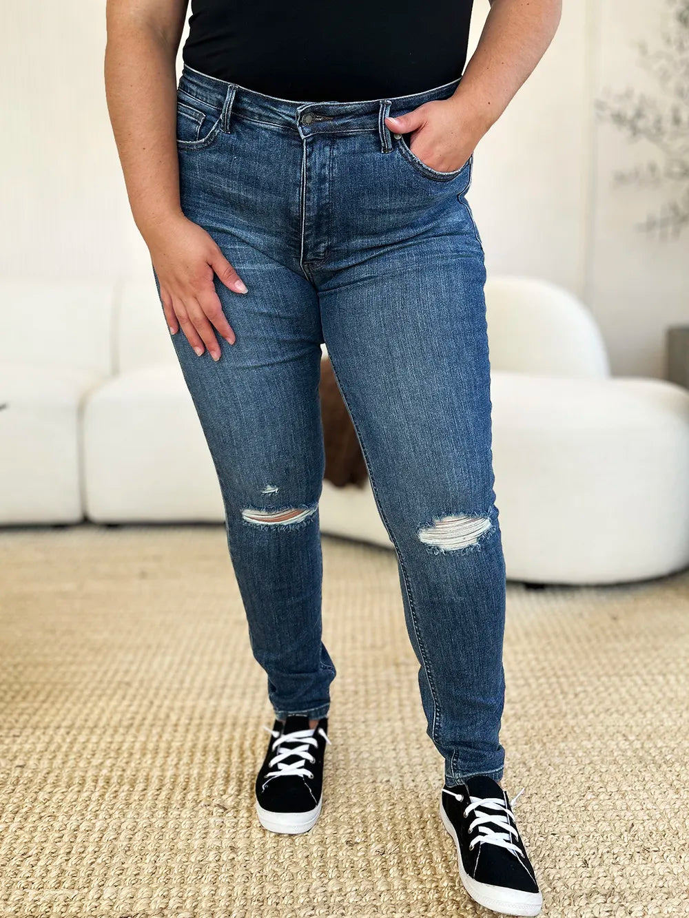 Person wearing blue jeans with slight distressing, standing on a carpeted floor.