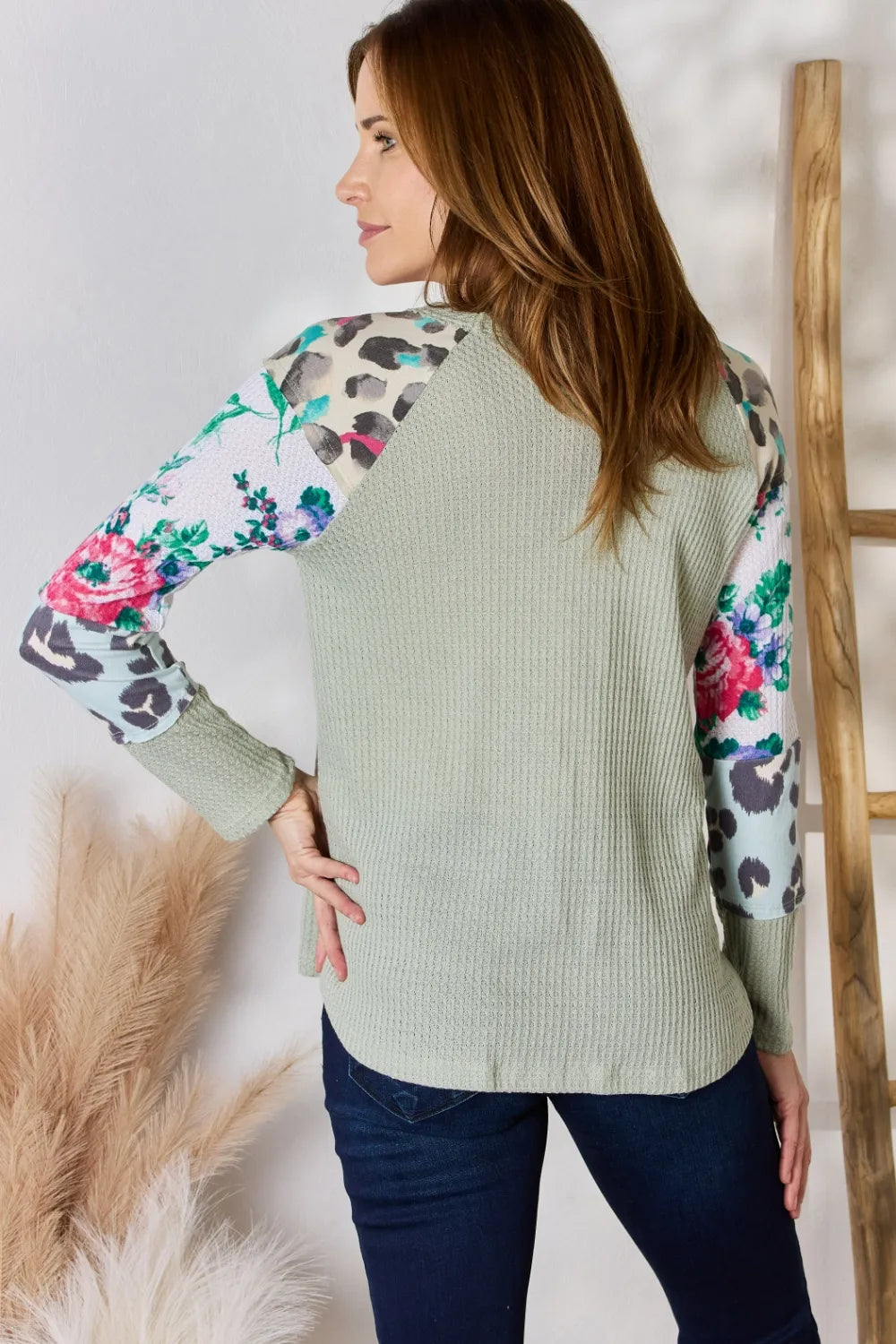 Woman wearing a light green sweater with floral and leopard print sleeves against a white background.