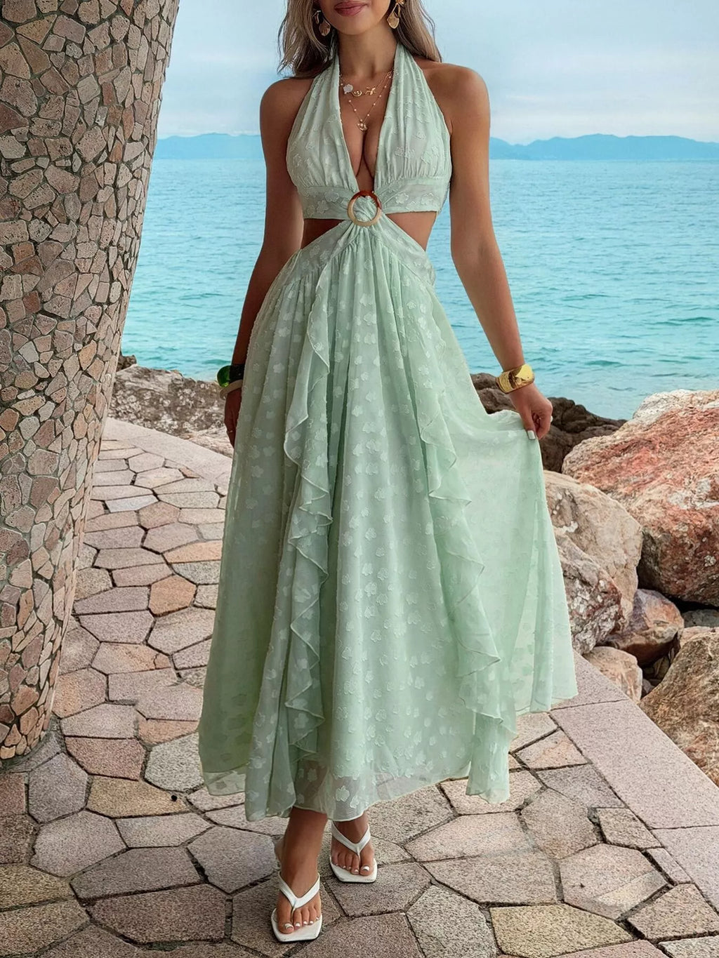 Woman in a light green dress standing by a stone wall with ocean view
