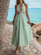 Woman in a light green dress standing by a stone wall with ocean view