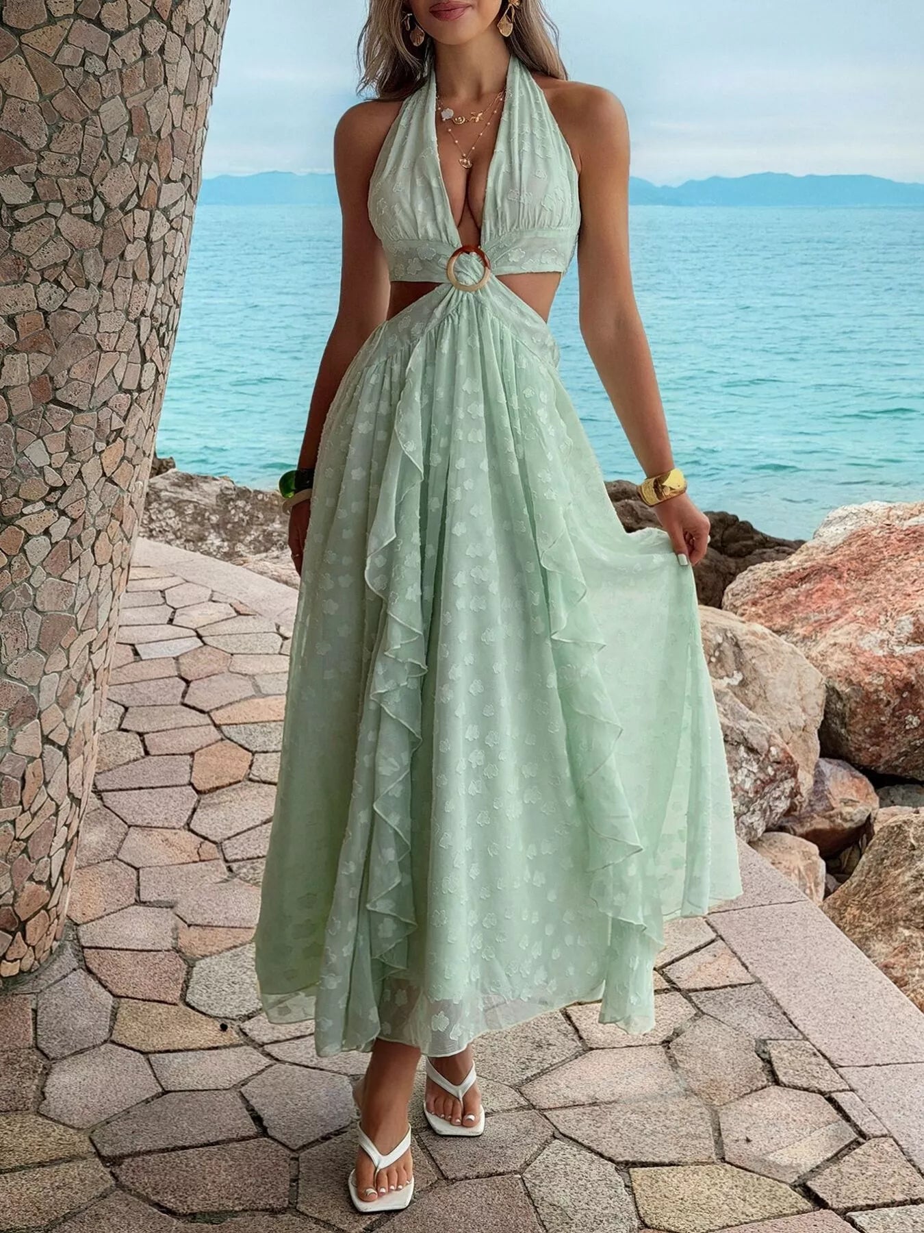 Woman in a light green dress standing by a stone wall with ocean view