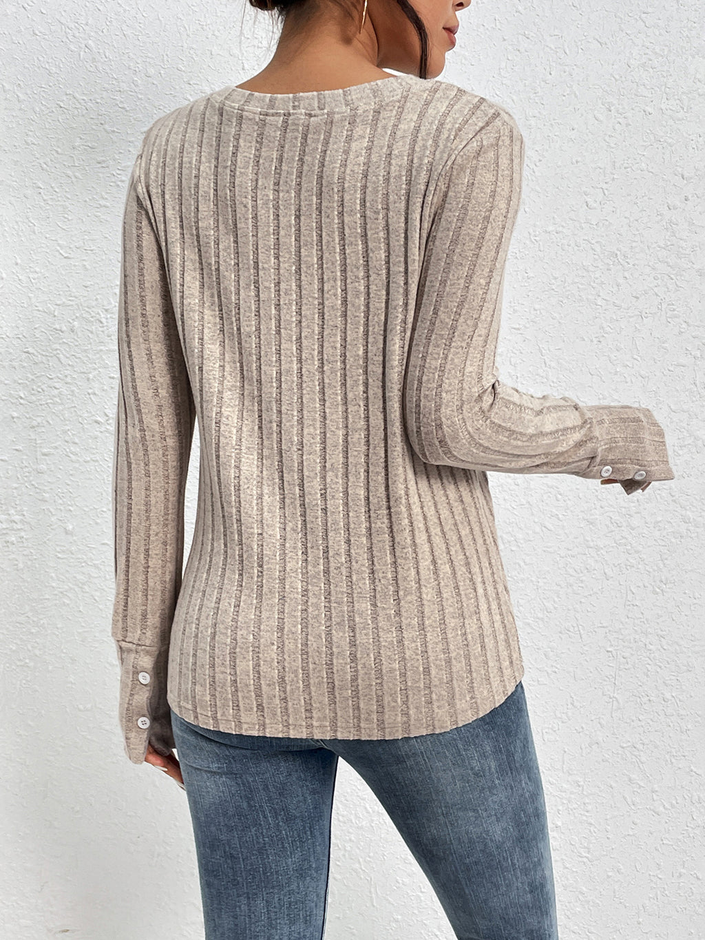 Person wearing a beige ribbed sweater and blue jeans against a white background