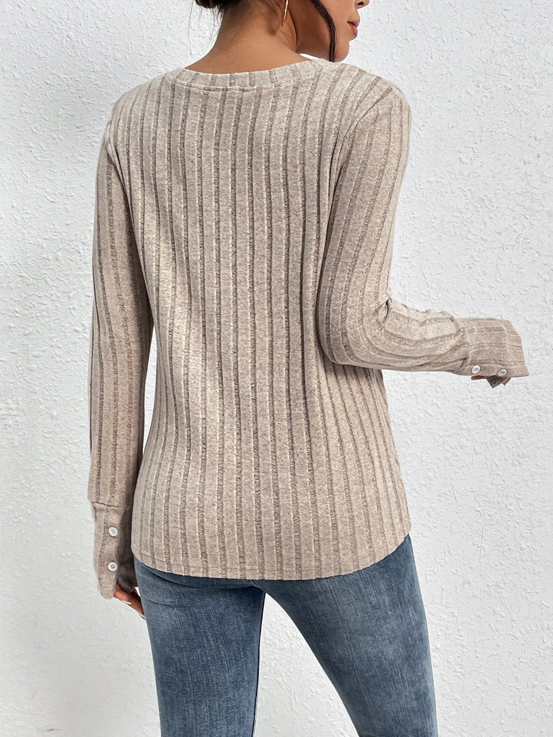 Person wearing a beige ribbed sweater and blue jeans against a white background