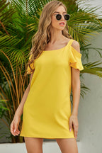 Woman wearing a yellow dress with ruffled sleeves in front of green foliage.
