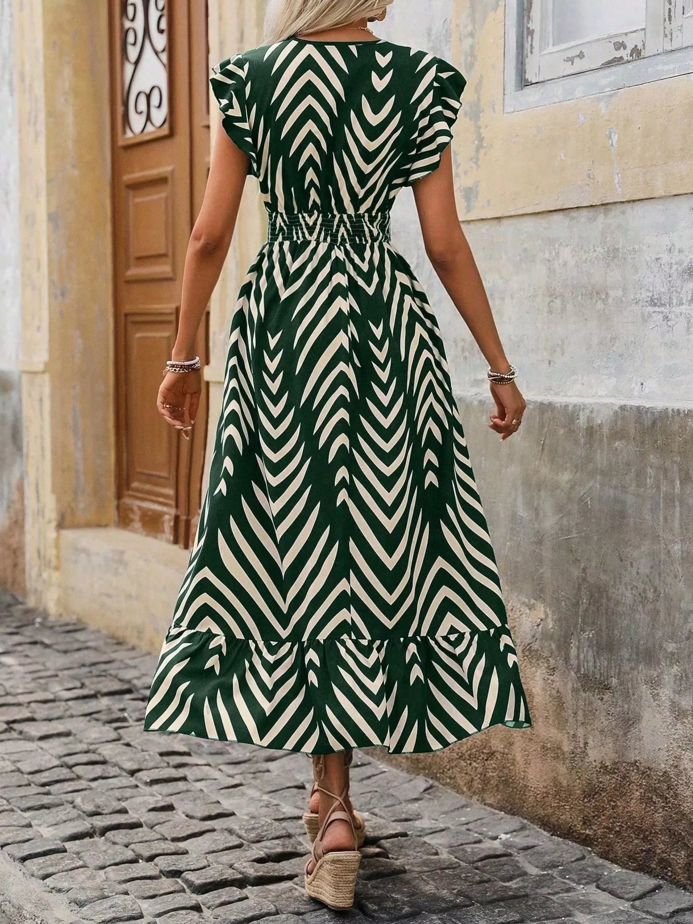 Woman wearing a green and white patterned dress walking on a cobblestone street.