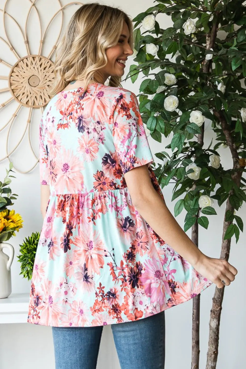 Woman wearing a floral dress standing next to a plant indoors
