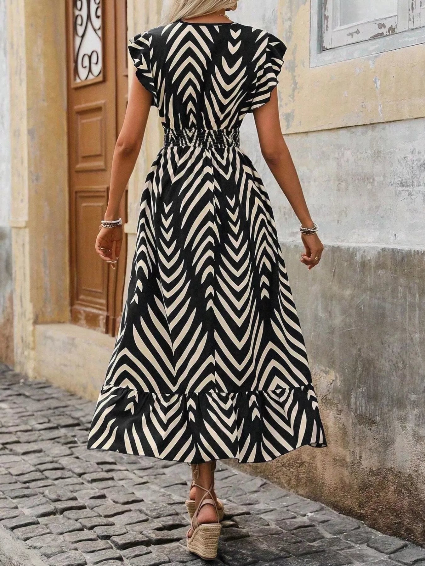 Woman wearing a black and white patterned dress walking on a cobblestone street.