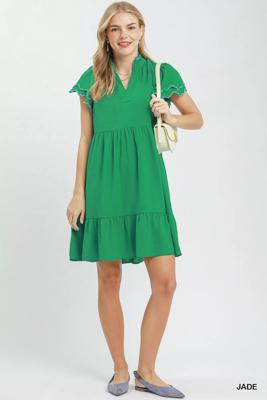 Woman wearing a green dress holding a beige handbag on a white background