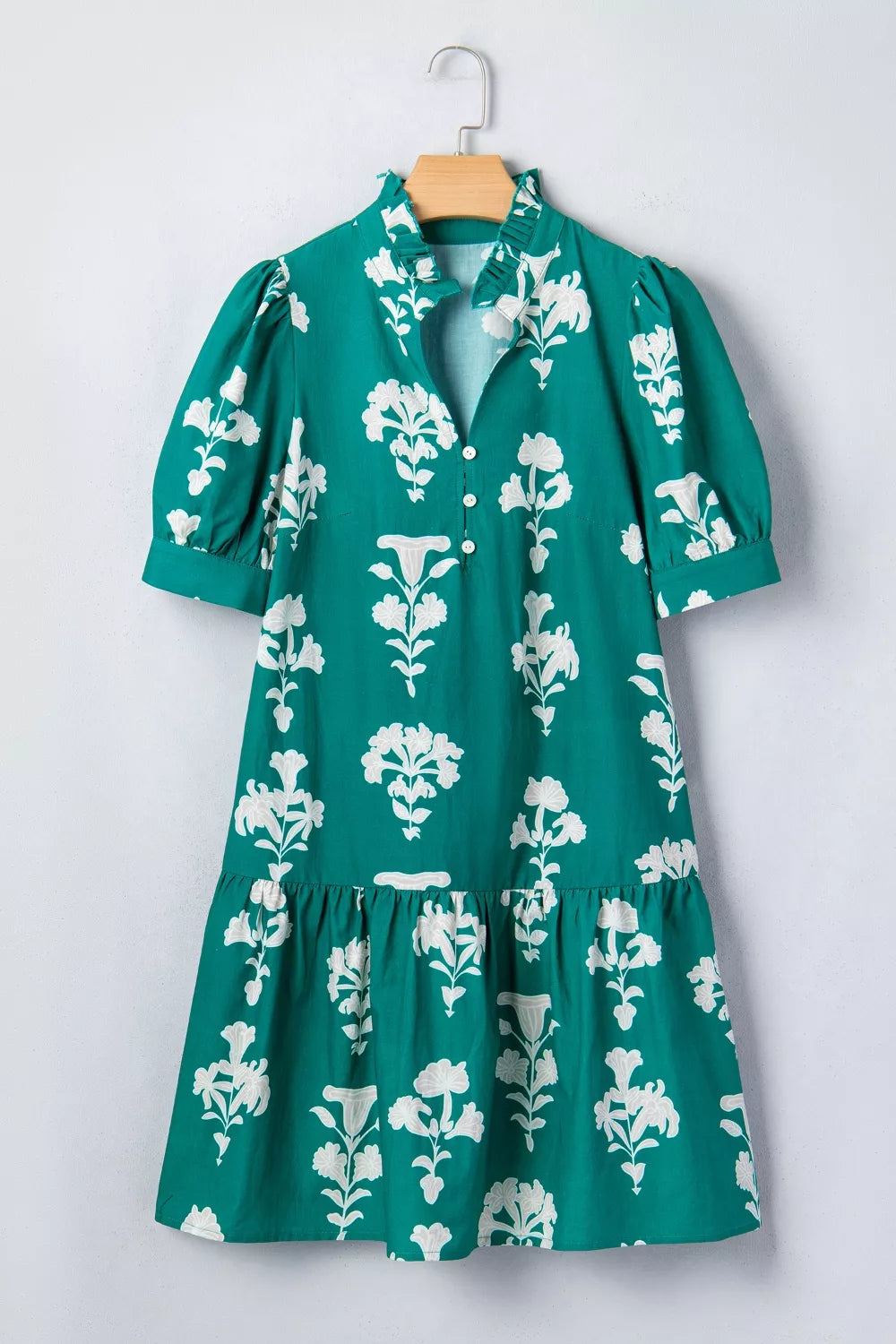 Green dress with white floral pattern on a hanger against a white background