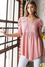 Woman wearing a pink blouse with puff sleeves in an indoor setting.