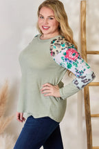Woman wearing a green sweater with floral and leopard print sleeves against a neutral background