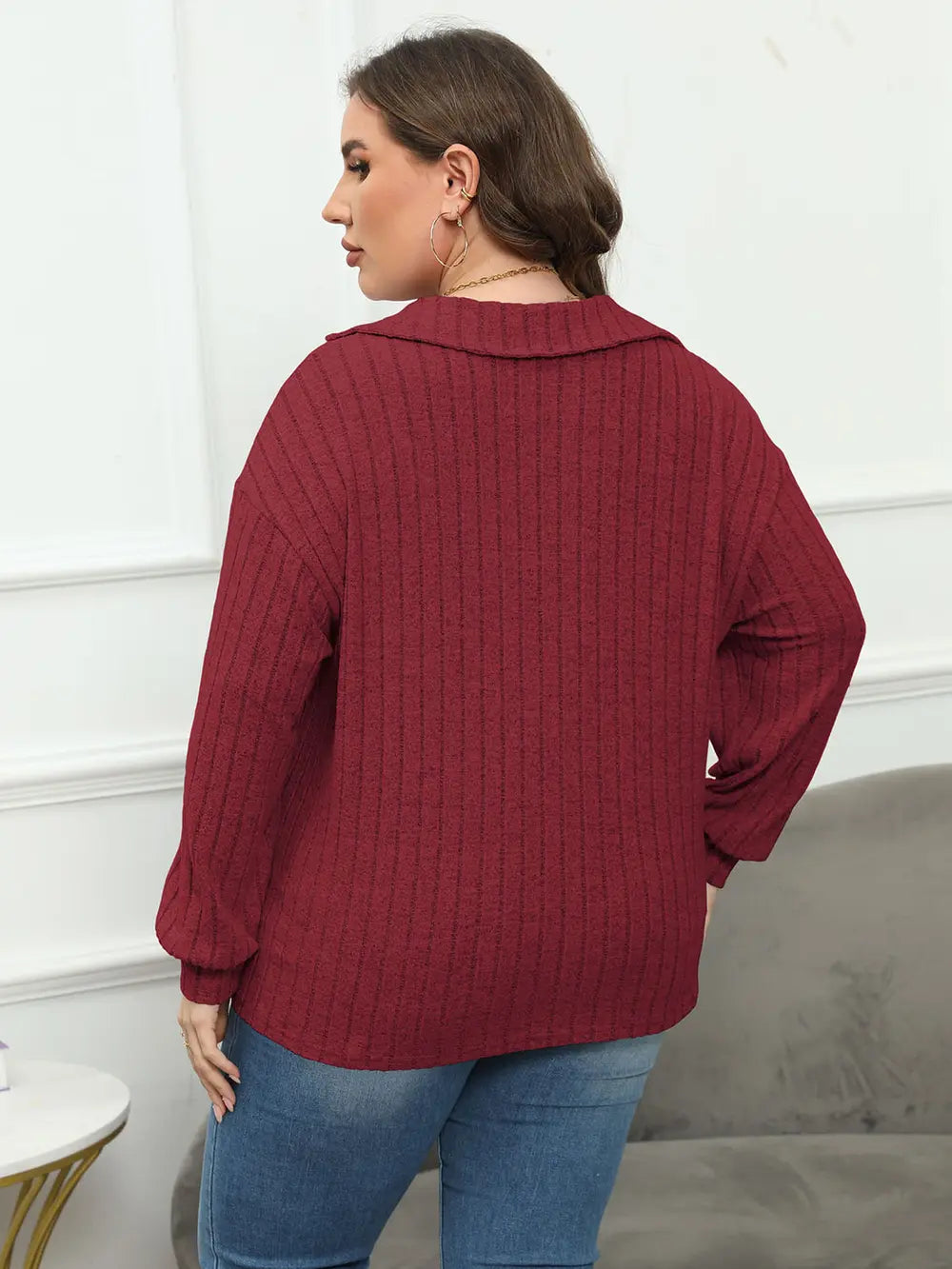Woman wearing a burgundy ribbed sweater and blue jeans in a minimal indoor setting