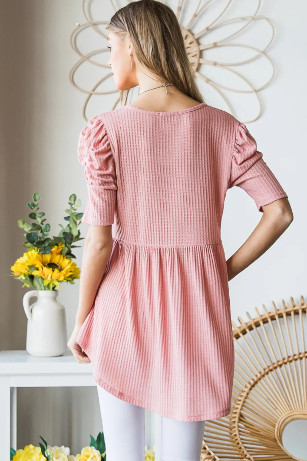 Woman wearing a pink dress standing in a room with decorative elements.