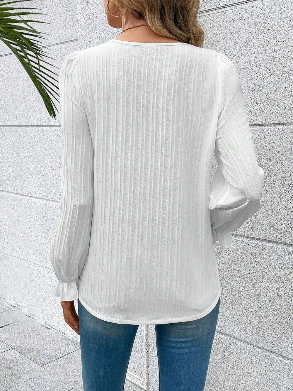 Person wearing a white ribbed blouse with long sleeves against a light gray wall.