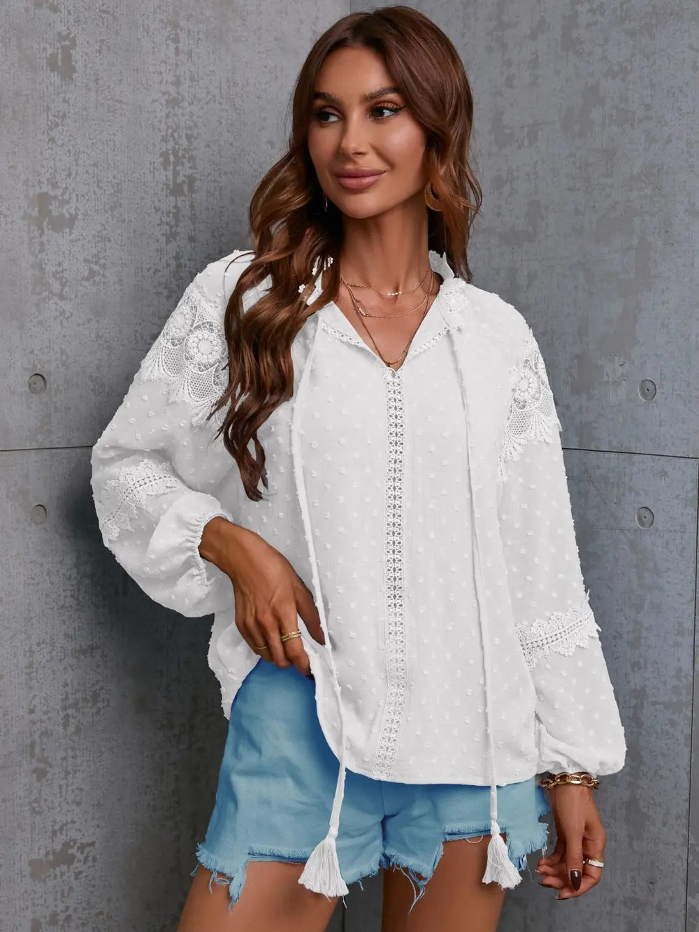 Woman wearing a white embroidered blouse and denim shorts against a gray wall.