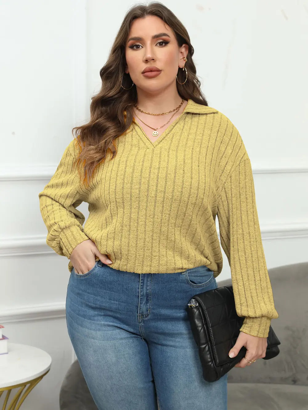 Woman wearing a yellow ribbed sweater and blue jeans, holding a black clutch.