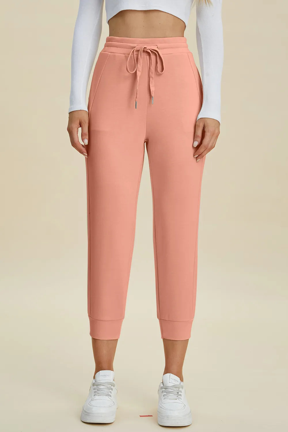 Person wearing pink sweatpants and white sneakers on a beige background