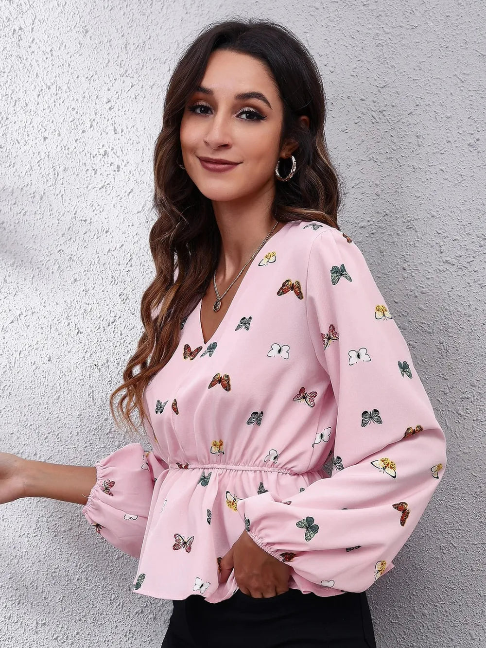 Woman wearing a pink blouse with butterfly pattern against a gray wall
