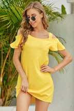Woman wearing a yellow dress with ruffled sleeves and sunglasses, standing in front of green plants.