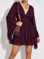 Person wearing a burgundy dress holding a brown leather bag against a white background