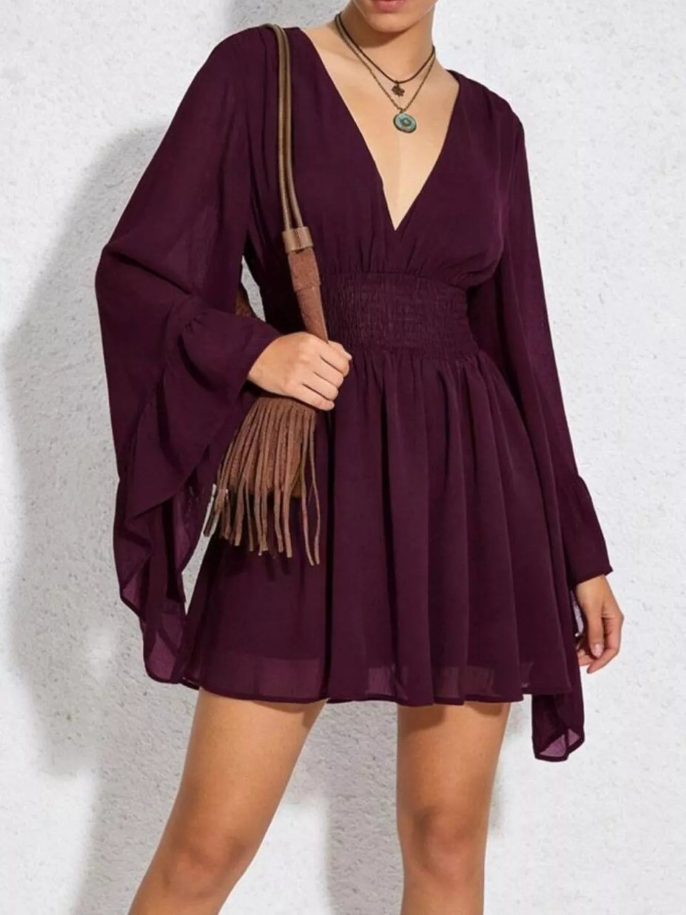 Person wearing a burgundy dress holding a brown leather bag against a white background
