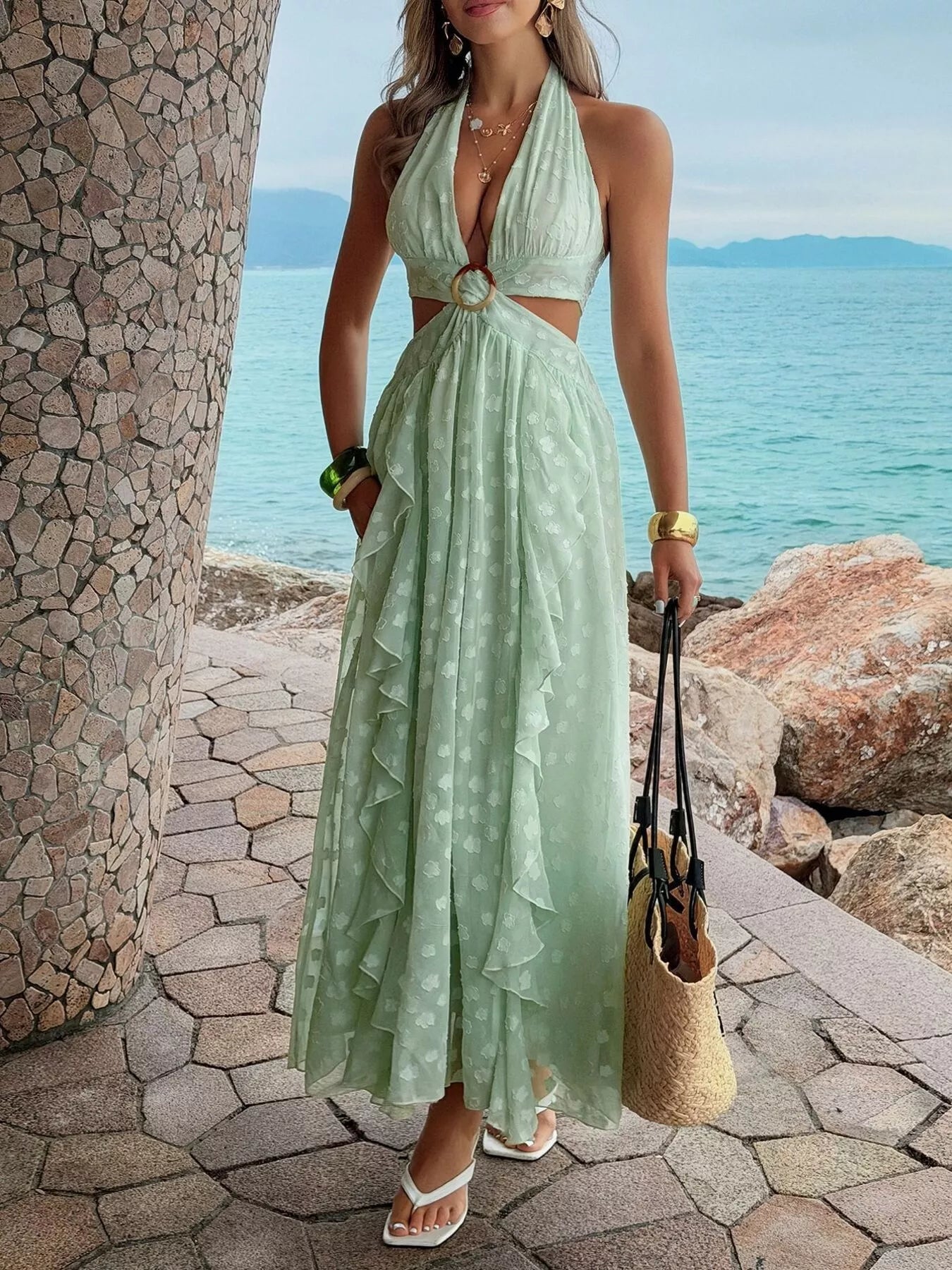 Woman in a light green dress standing by a stone wall with ocean view