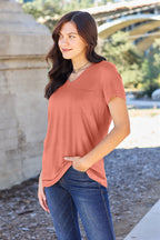 Woman wearing a peach-colored top and blue jeans standing outdoors with a blurred background